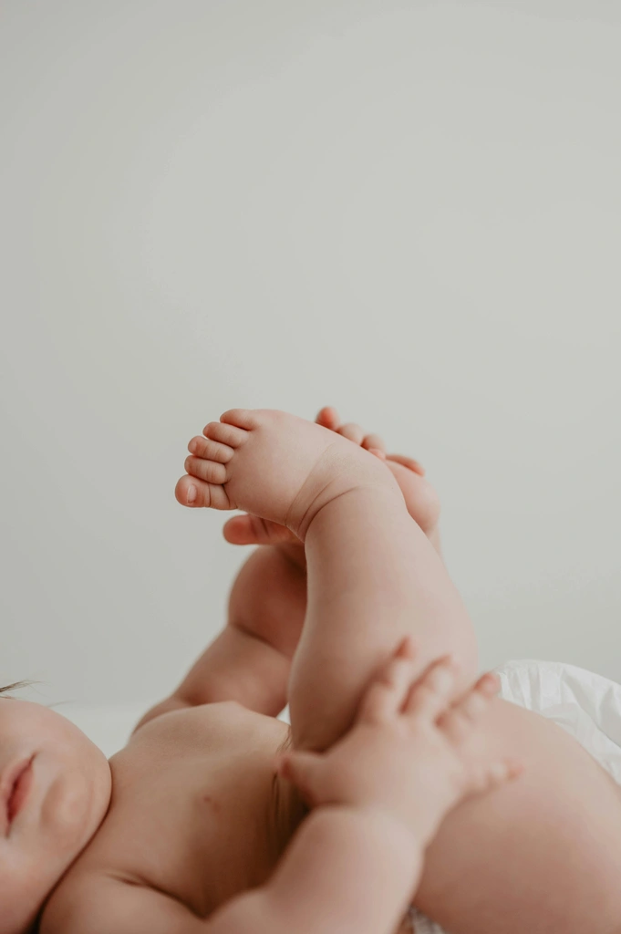 Baby liegt auf dem Ruecken und haelt die Fuesse fest
