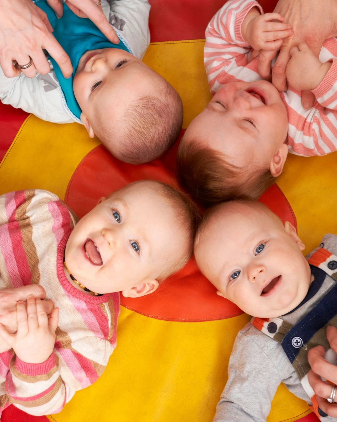 Vier Babies liegen auf dem Ruecken und strahlen in die Kamera